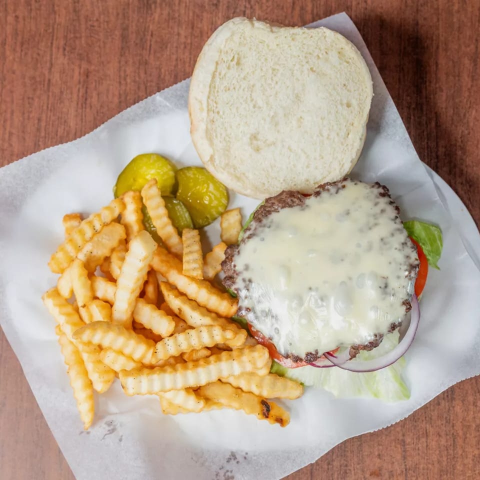 Cheeseburger with melted cheese, open bun, crinkle-cut fries, and pickles on white paper.