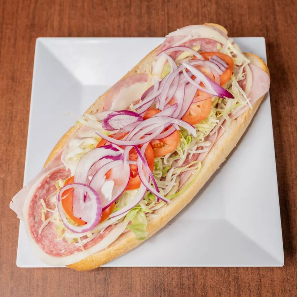 Overhead view of a loaded sub sandwich with salami, ham, cheese, lettuce, tomatoes, and red onions.
