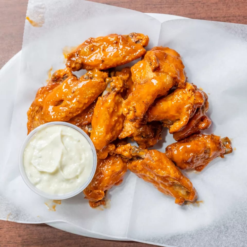 A serving of glistening orange buffalo wings with a small cup of ranch dressing.
