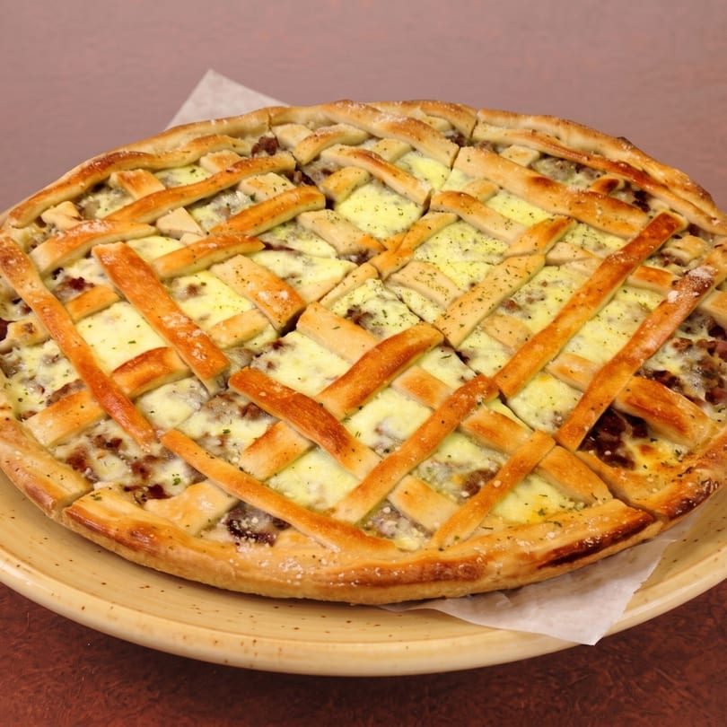 A freshly baked pizza with a lattice crust, cheese, and meat, served on a yellow plate.