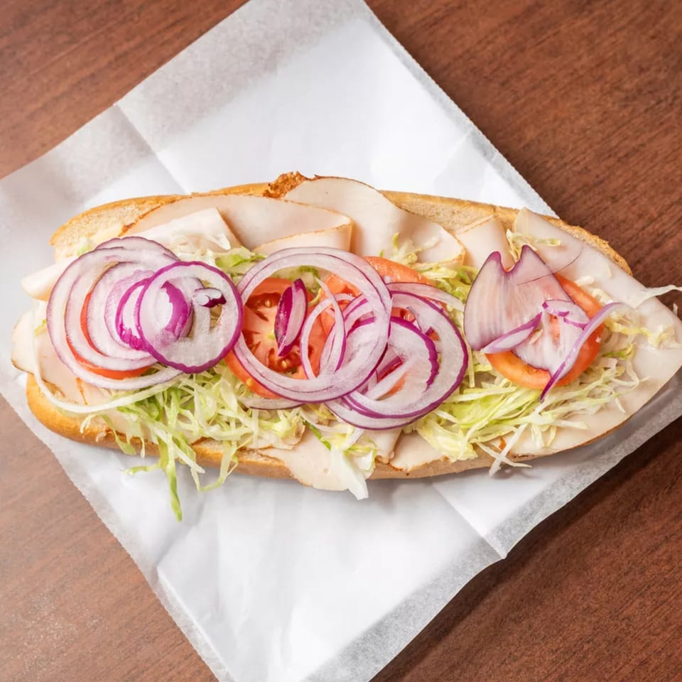 Turkey sub sandwich with shredded lettuce, sliced tomatoes, and red onions on white paper.
