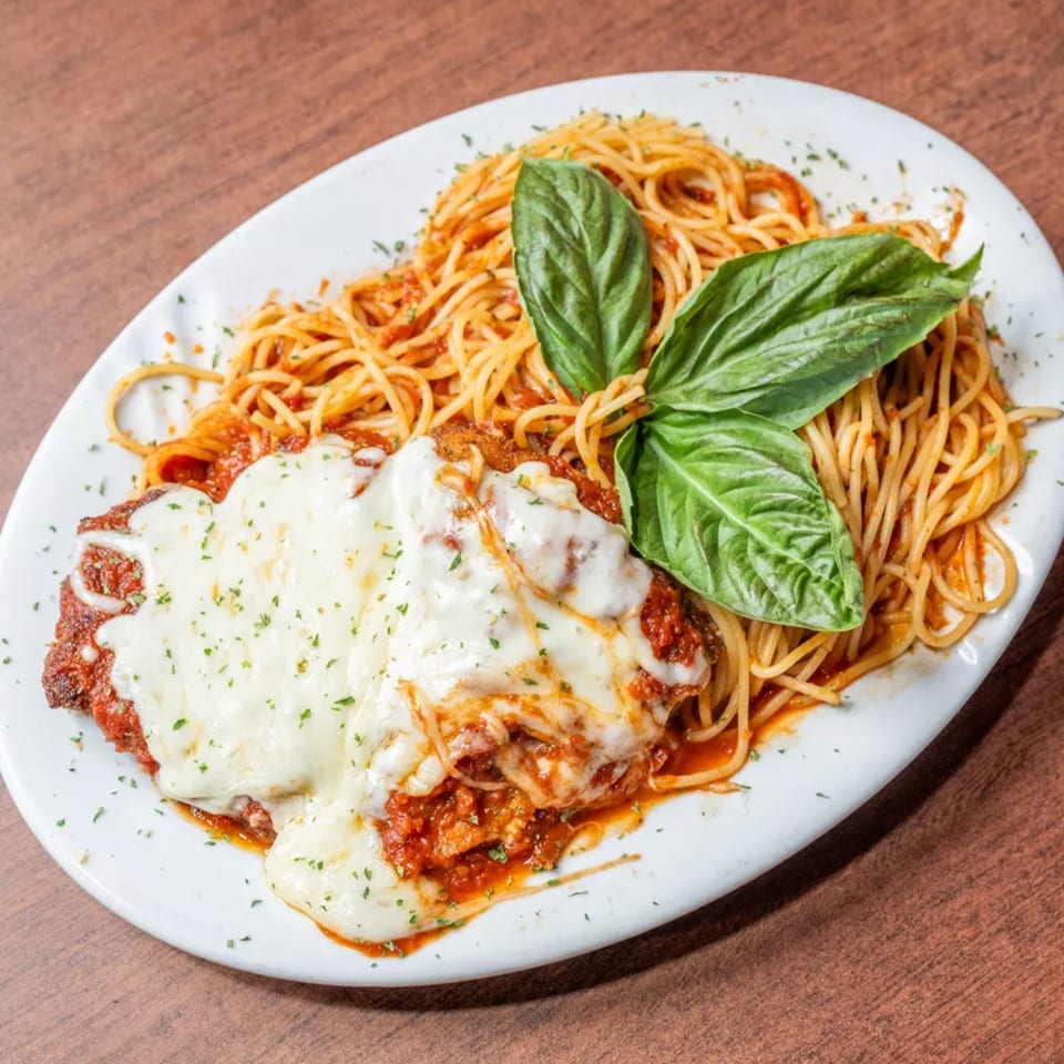 Chicken parmesan with melted cheese and spaghetti, garnished with fresh basil.
