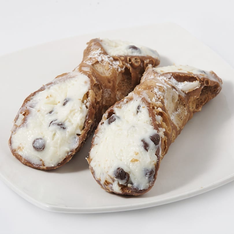 Two cannoli with white cream filling and chocolate chips, dusted with powdered sugar on a white plate.
