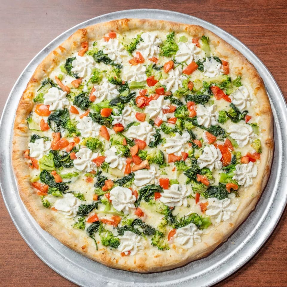 White pizza with broccoli, spinach, diced tomatoes, and ricotta cheese on a metal pan.