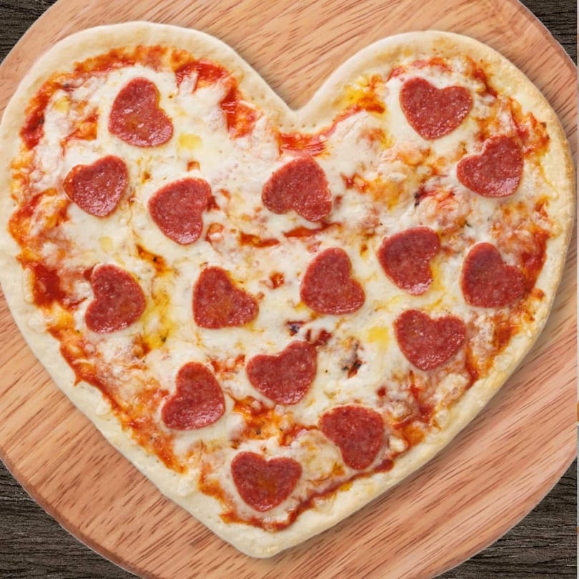 Heart-shaped pizza with heart-shaped pepperoni slices on a wooden board.